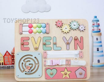 May include: Wooden educational toy with the name "EVELYN" spelled out in colorful letters. Features include a maze, zipper, buckle, gears, and shape sorter. The toy is designed for early childhood development and learning.