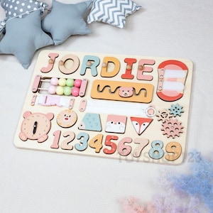K&ouml;nnte beinhalten: Holz-Lernpuzzle-Tafel mit dem Namen "JORDIE" in bunten Buchstaben. Enth&auml;lt einen Abakus, eine Uhr, die Zahlen 1-9 und Tierformen. Das Brett ist f&uuml;r fr&uuml;hes Lernen und Entwicklung konzipiert.