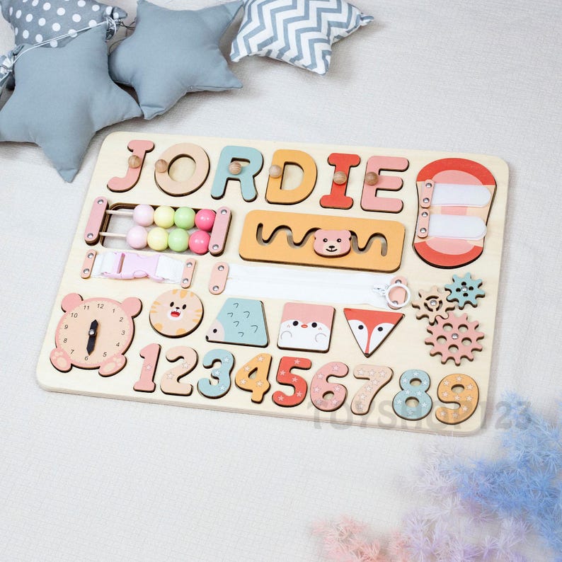 K&ouml;nnte beinhalten: Holz-Lernpuzzle-Tafel mit dem Namen "JORDIE" in bunten Buchstaben. Enth&auml;lt einen Abakus, eine Uhr, die Zahlen 1-9 und Tierformen. Das Brett ist f&uuml;r fr&uuml;hes Lernen und Entwicklung konzipiert.