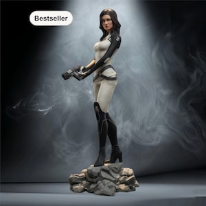 May include: A detailed figurine of a woman in a futuristic white and black outfit, holding a gun. The figure stands on a rocky base, with a "Bestseller" label in the upper left corner. The background is a smoky gray.
