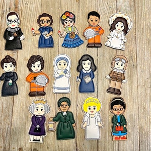 May include: A collection of colorful felt cutouts depicting notable women, including a judge, scientist, artist, astronaut, and others. Each figure is detailed with unique clothing and accessories, set against a light wood grain background.