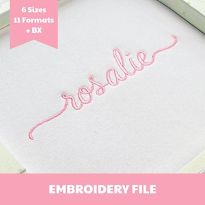 May include: A white fabric surface featuring the pink embroidered name rosalie in a cursive script font. A pink banner in the upper left corner displays the text 6 Sizes 11 Formats + BX, and a pink bar at the bottom contains the text EMBROIDERY FILE.