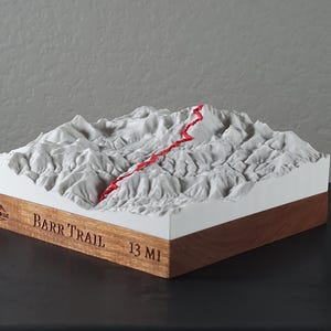 May include: A 3D topographical model of the Barr Trail, featuring a red trail line winding through the white mountain terrain. The base is wood, with the text "BARR TRAIL 13 MI".