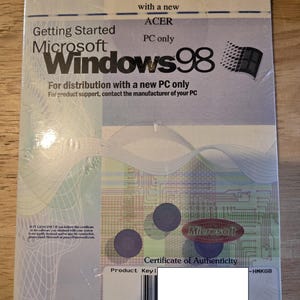 Op de afbeelding: Verzegeld Microsoft Windows 98 softwarepakket. Het pakket is verpakt in doorzichtig plastic en bevat het Windows 98-logo, de tekst "Getting Started" en een certificaat van echtheid. Het pakket is alleen voor distributie met een nieuwe ACER pc.