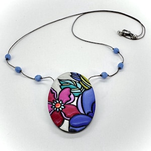 Pode incluir: Um colar com pingente floral com um cordão preto e contas azuis. O pingente oval apresenta um design vibrante de flores vermelhas, rosa e azuis com folhas verdes e amarelas. O colar é uma peça de joalheria única.