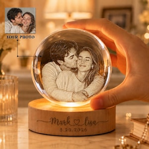 Könnte beinhalten: Personalisierte Kristallkugel mit Foto eines küssenden Paares. Sie steht auf einem Holzsockel mit den Namen "Mark & Lisa" und dem Datum "5.20.2026" eingraviert. Die Worte "YOUR PHOTO" sind oben links sichtbar. Die Kugel ist beleuchtet.