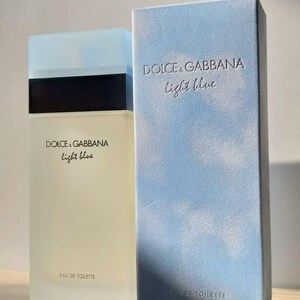 Puede incluir: Un juego de botella y caja de perfume. La botella es rectangular con una tapa azul claro y una banda negra. La caja es azul claro con las palabras "DOLCE & GABBANA light blue" impresas tanto en la botella como en la caja. Las palabras "EAU DE TOILETTE" también están impresas en la botella.