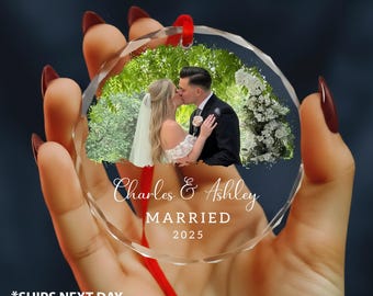 May include: Clear, faceted glass ornament with a photo of a kissing couple, greenery, and white flowers. The ornament has the names "Charles & Ashley" and the word "MARRIED" with the year "2025" in white script.