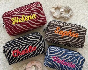 Puede incluir: Cuatro estuches rectangulares con cremallera y estampado de cebra en rojo, marrón, negro y azul. Cada estuche tiene un nombre bordado: Helena en amarillo, Sophia en naranja, Charlie en rojo y Victoria en rosa. Incluye dos coleteros beige.