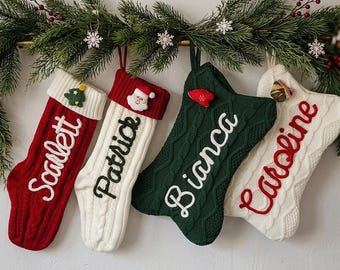 Puede incluir: Cuatro calcetines navideños de punto trenzado colgados en fila. El primero es rojo con el texto blanco Scarlett, el segundo es blanco con el texto verde Patrick, el tercero es verde oscuro con el texto blanco Bianca y el cuarto es blanco con el texto rojo Caroline.