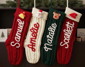 Puede incluir: Cuatro calcetines navideños de punto trenzado colgados en fila. El primero es rojo con una campana amarilla y el nombre Samuel. El segundo es blanco con una cara de Santa y el nombre Amelie. El tercero es verde con un reno y el nombre Natalie. El cuarto es rojo con un gorro de Santa y el nombre Scarlett.