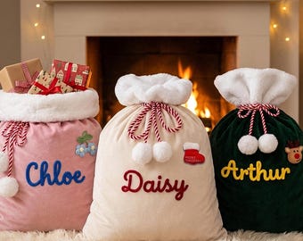 Puede incluir: Tres sacos de regalo navideños de tela con borde de piel sintética blanca y cierre de cordón. El saco rosa está bordado con "Chloe", el crema con "Daisy" y el verde oscuro con "Arthur". Cada uno tiene parches festivos.