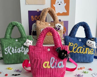 Puede incluir: Cuatro bolsos tote de pana en verde, beige, rosa y azul, cada uno con cierre de botón a presión blanco, dos asas y una correa para el hombro. Los bolsos están personalizados con los nombres bordados Kristy, Malia y Claine, y decorados con pequeños dijes de peluche con temática de Halloween.