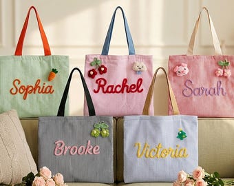 Puede incluir: Cinco bolsos de tela de pana con nombres bordados y pequeñas aplicaciones de peluche. Los bolsos son verde claro con asas naranjas, rosa con asas azules, rosa claro con asas beige, gris a rayas con asas negras y azul con asas beige.