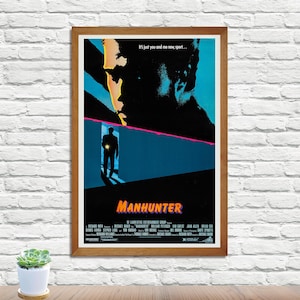 Puede incluir: Póster enmarcado de la película "Manhunter" con un diseño oscuro y estilizado. El póster presenta la silueta de una persona en una puerta, una cara grande y el título en naranja. El texto "It's just you and me now, sport..." está en la parte superior.