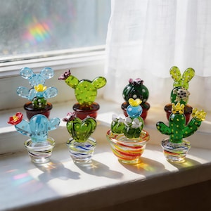 Puede incluir: Colecci&oacute;n de esculturas de cactus de vidrio de colores en varias formas y tama&ntilde;os. Los cactus est&aacute;n en macetas peque&ntilde;as, algunas con dise&ntilde;os a rayas. El vidrio es transparente, con detalles como flores y espinas.