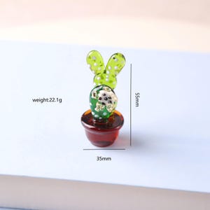 Puede incluir: Figura de cactus de cristal en una maceta roja. El cactus verde tiene lunares blancos y mide 5,5 cm de alto y 3,5 cm de ancho. La figura pesa 22,1 g. El cactus tiene dos estructuras verdes en forma de hoja en la parte superior.