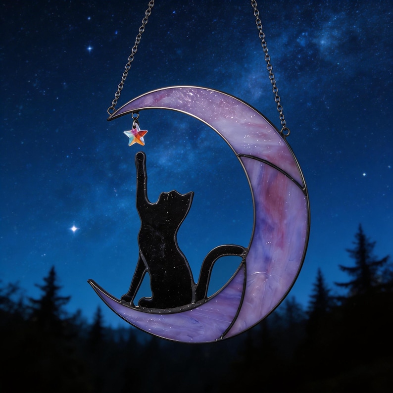 May include: A stained glass suncatcher featuring a crescent moon in shades of purple and white, with a black cat silhouette sitting on the moon and reaching up towards a small, iridescent, multi-coloured star hanging from the top curve.