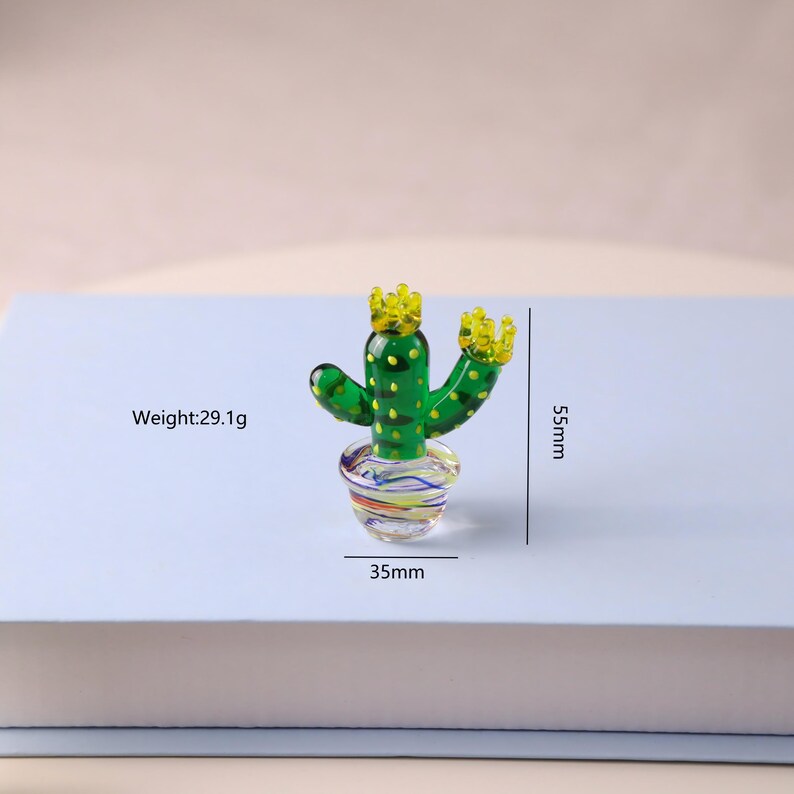 Puede incluir: Una figura de cactus de vidrio verde con detalles amarillos en forma de corona. El cactus est&aacute; en una maceta de vidrio colorida. La figura mide 5,5 cm de alto y 3,5 cm de ancho. El peso es de 29,1 g.
