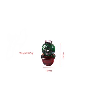 Puede incluir: Una figura de cactus de cristal en miniatura. El cactus verde tiene detalles blancos y est&aacute; colocado en una maceta de color rojo oscuro. La figura mide 4,5 cm de alto y 3,5 cm de ancho, con un peso de 33,5 g.