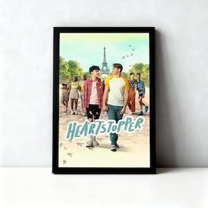 May include: A framed poster featuring the title "Heartstopper" in light blue script. The image depicts a group of people walking, with the Eiffel Tower in the background. The poster is in a black frame.