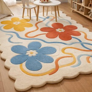 May include: A cream-colored, scalloped-edge rug with a floral design. The rug features three large flowers in yellow, orange, and blue, with white centers. Wavy lines in blue, orange, and yellow connect the flowers. A playful and colorful addition to any room.