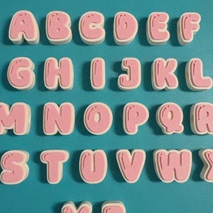 May include: A set of three-dimensional alphabet letters arranged in rows. Each letter features a light pink, rounded, bubble-style front surface with a white base layer. The letters are displayed in alphabetical order from A to Z.