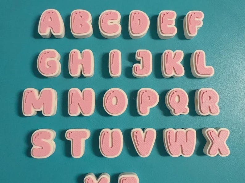 May include: A set of three-dimensional alphabet letters arranged in rows. Each letter features a light pink, rounded, bubble-style front surface with a white base layer. The letters are displayed in alphabetical order from A to Z.