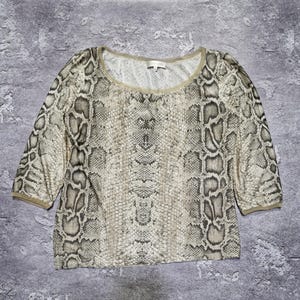 May include: A short-sleeved top with a snakeskin pattern in shades of beige, gray, and brown. The top has a round neckline and the sleeves end just below the elbow. The fabric appears to be lightweight.