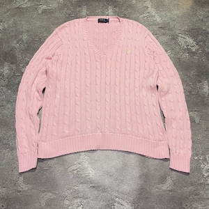 May include: A light pink long-sleeve V-neck sweater featuring a vertical cable knit pattern. The garment has a ribbed hem and cuffs, with a small embroidered logo on the left chest and a Polo Ralph Lauren label at the inner neckline.