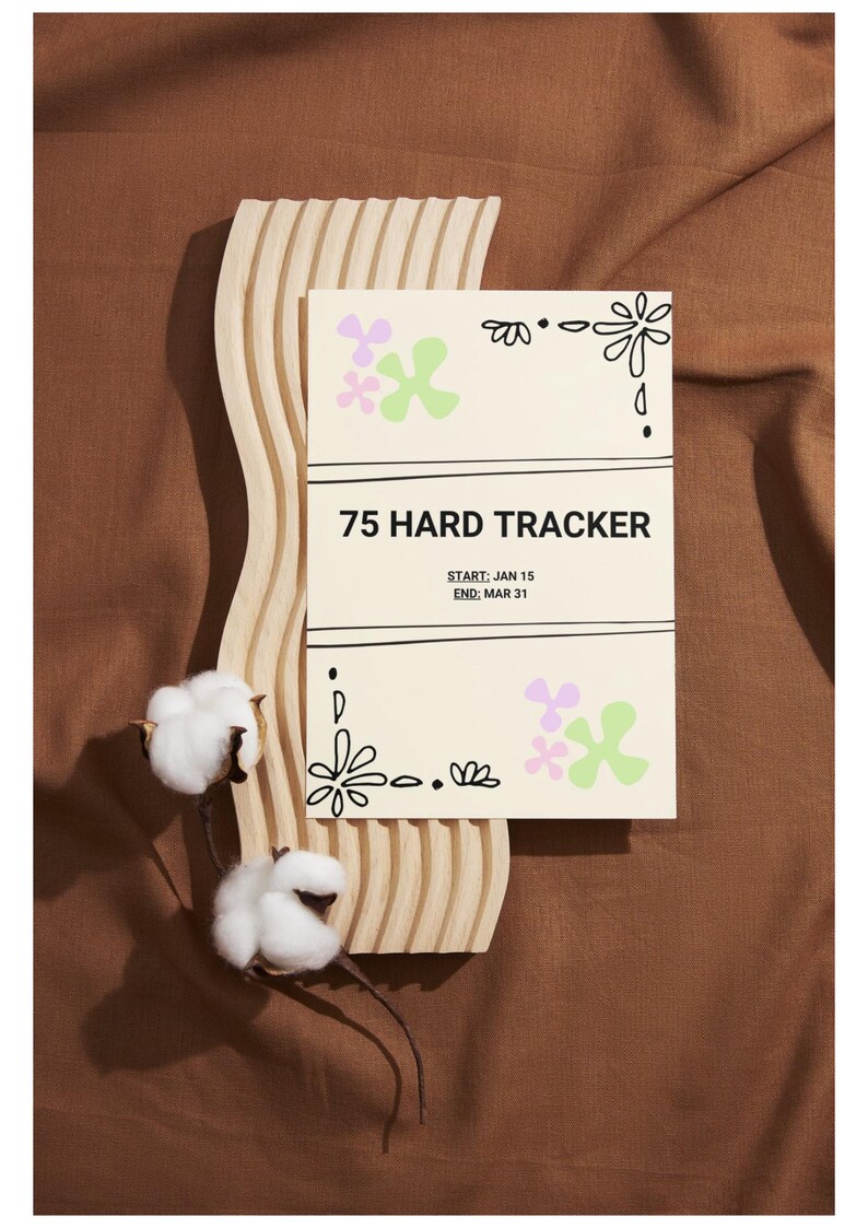 May include: A cream-coloured 75 Hard Tracker card with floral designs and the start and end dates of the challenge. The card is propped up on a wooden, wavy, decorative piece, with cotton stems in the foreground.