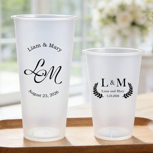 Könnte beinhalten: Zwei mattierte Plastikbecher mit individuellem Text und Datum, einer hoch und einer kürzer, stehen auf einem Holztablett. Auf dem hohen Becher steht "Liam & Mary" über "LM" und "August 23, 2026". Der kleinere Becher hat "L&M" mit "Liam and Mary" und "5.23.2026."
