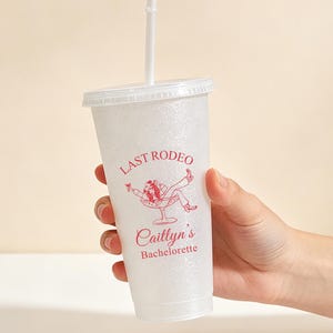 K&ouml;nnte beinhalten: Ein klarer, glitzerbedeckter Plastikbecher mit wei&szlig;em Deckel und Strohhalm. Der Becher tr&auml;gt den roten Aufdruck "LAST RODEO" und "Caitlyn's Bachelorette" sowie eine Grafik einer Person, die sich in einem Cocktailglas zur&uuml;cklehnt.