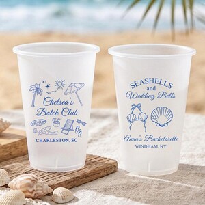 May include: Two frosted plastic cups with blue ink designs. The left cup features palm trees, a beach umbrella, and the text "Chelsea's Batch Club CHARLESTON, SC". The right cup displays seashells and the text "SEASHELLS and Wedding Bells Anna's Bachelorette WINDHAM, NY".