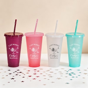 K&ouml;nnte beinhalten: Vier glitzernde Plastikbecher mit Deckeln und Strohhalmen. Jeder Becher hat eine andere Farbe: Dunkelrosa, Hellrosa, Klar und T&uuml;rkis. Der Text "LAST RODEO" und "Caitlyn's Bachelorette" ist auf jedem Becher aufgedruckt.