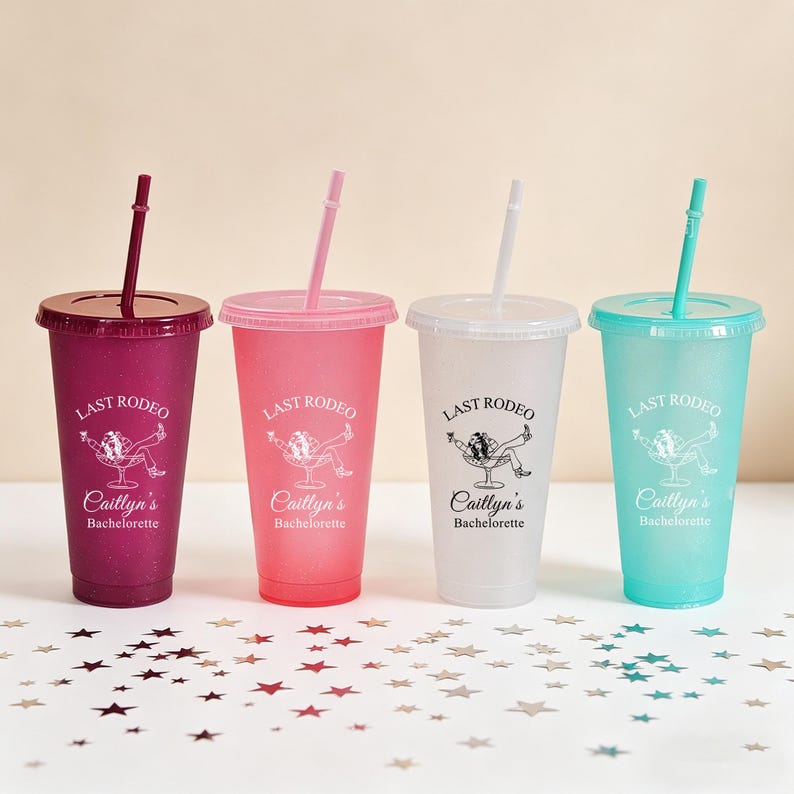 K&ouml;nnte beinhalten: Vier glitzernde Plastikbecher mit Deckeln und Strohhalmen. Jeder Becher hat eine andere Farbe: Dunkelrosa, Hellrosa, Klar und T&uuml;rkis. Der Text "LAST RODEO" und "Caitlyn's Bachelorette" ist auf jedem Becher aufgedruckt.