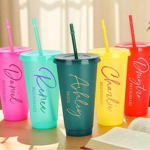 May include: Five colorful tumblers with lids and straws. Each tumbler is a different color: pink, teal, green, yellow, and red. The tumblers have names printed on them in a cursive font, with the word "Bridesmaid" or "Bride" below.