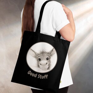 May include: Black tote bag featuring a circular illustration of a donkey's face with large eyes and floppy ears. The text "Good Stuff" is printed below the illustration in a cursive font. The bag has black handles.