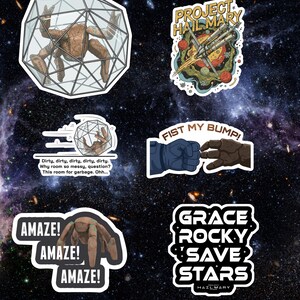 May include: A collection of white-bordered stickers with space-themed designs. The stickers feature illustrations of a space station, a creature in a cage, and text including "Project Hail Mary", "Fist My Bump!", and "Amaze!"
