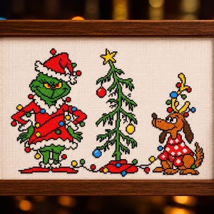 May include: A cross-stitch embroidery in a dark wood frame featuring a green character in a red Santa suit, a sparse Christmas tree with colorful ornaments, and a brown dog wearing a red sweater with antlers, all connected by a string of lights.