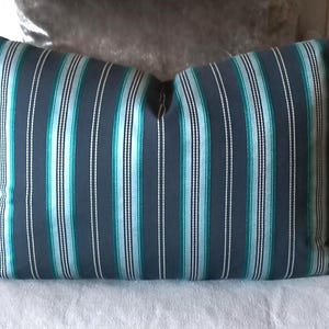 May include: A rectangular cushion featuring a striped design in navy, teal, and white. The cushion is placed on a light grey surface. The vertical stripes create a visually appealing design, suitable for home decor. The cushion is likely filled with feathers or a synthetic alternative.