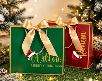 May include: Two rectangular gift bags, one green and one red, each featuring a gold satin ribbon bow, gold rope handles, and a small Santa hat graphic. The green bag displays the name Willow and the text MERRY CHRISTMAS in gold lettering.