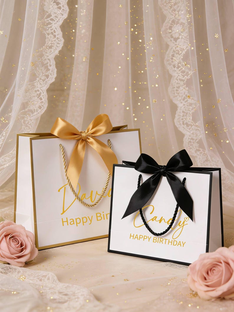 May include: Two white gift bags with gold trim and handles, each with a satin bow. One bag has a gold bow and the text "Happy Birthday" in gold script. The other bag has a black bow and the word "Candy" and "Happy Birthday" in gold script.