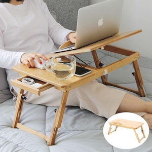Peut inclure: Un bureau d'ordinateur portable en bambou avec des pieds réglables et une surface inclinable. Le bureau comprend un petit tiroir, un porte-gobelet et un emplacement pour téléphone. Un ordinateur portable, une souris et un verre d'eau sont sur le bureau.