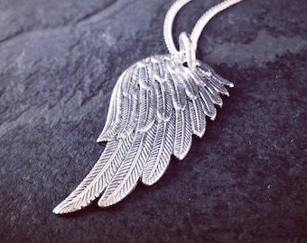 May include: A silver necklace with a detailed wing pendant. The wing is made of metal and has a textured surface.