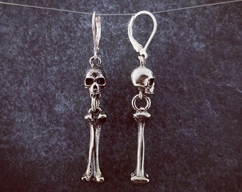 May include: A pair of silver skull and bone earrings. Each earring features a small skull charm with a bone dangle.