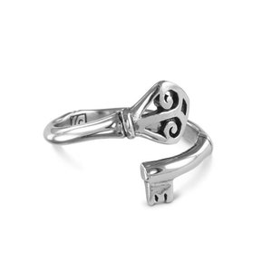 May include: A silver key-shaped ring with a detailed design on the key head. The ring is open and the key is bent to form the ring.