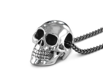 May include: A silver skull pendant necklace with a black chain. The skull is detailed with teeth and eye sockets.