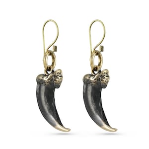May include: A pair of gold and black claw earrings. The claws are made of metal and have a realistic look. The earrings are hanging from gold hoops.