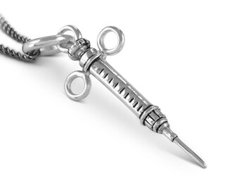May include: A silver-toned syringe pendant necklace. The syringe has a detailed design with a needle and a plunger. The pendant is attached to a silver chain.